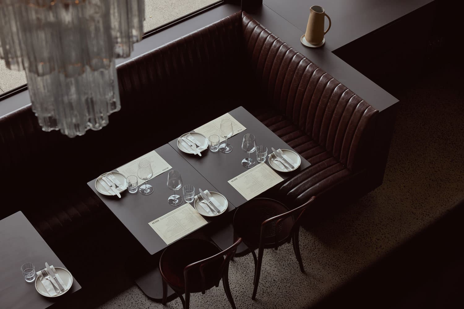A curved leather booth at Petite set for dinner, beside the window and under a vintage Murano chandelier