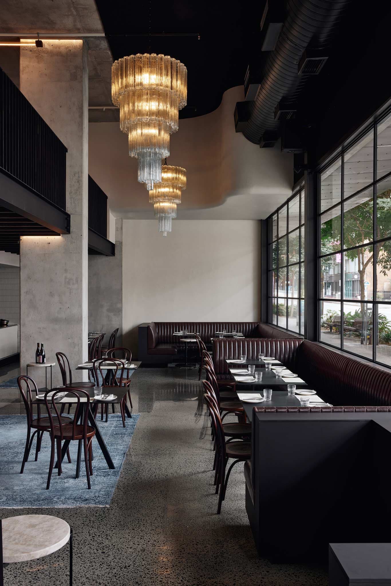 Petite's main dining room, with leather banquettes along the window, long tables and a vintage Murano chandelier