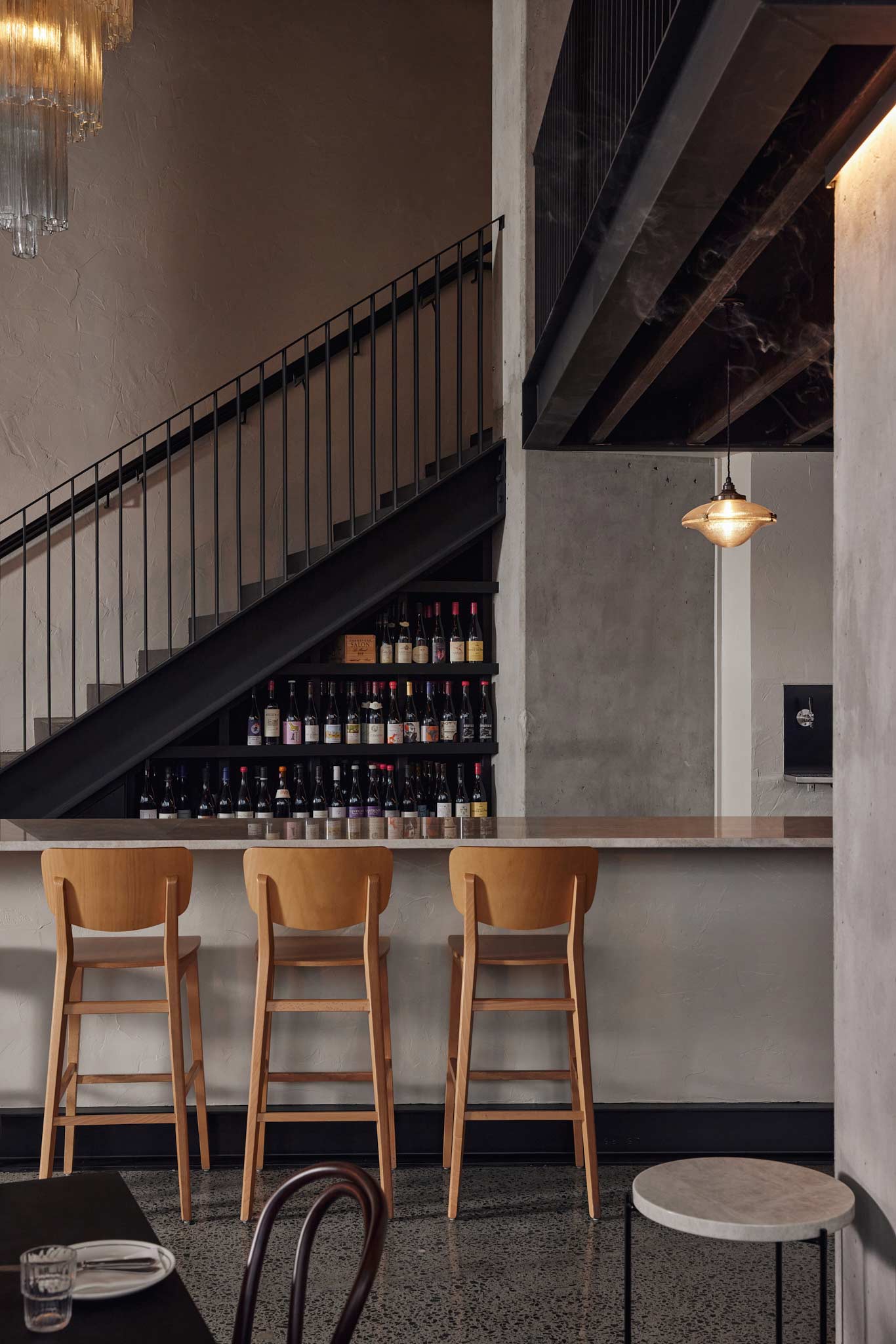 Petite's wine wall stacked with bottles beneath the mezzanine staircase, with stools at the granite bar